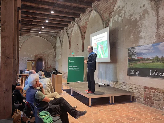 Interessierte hören einem Vortragendem zu