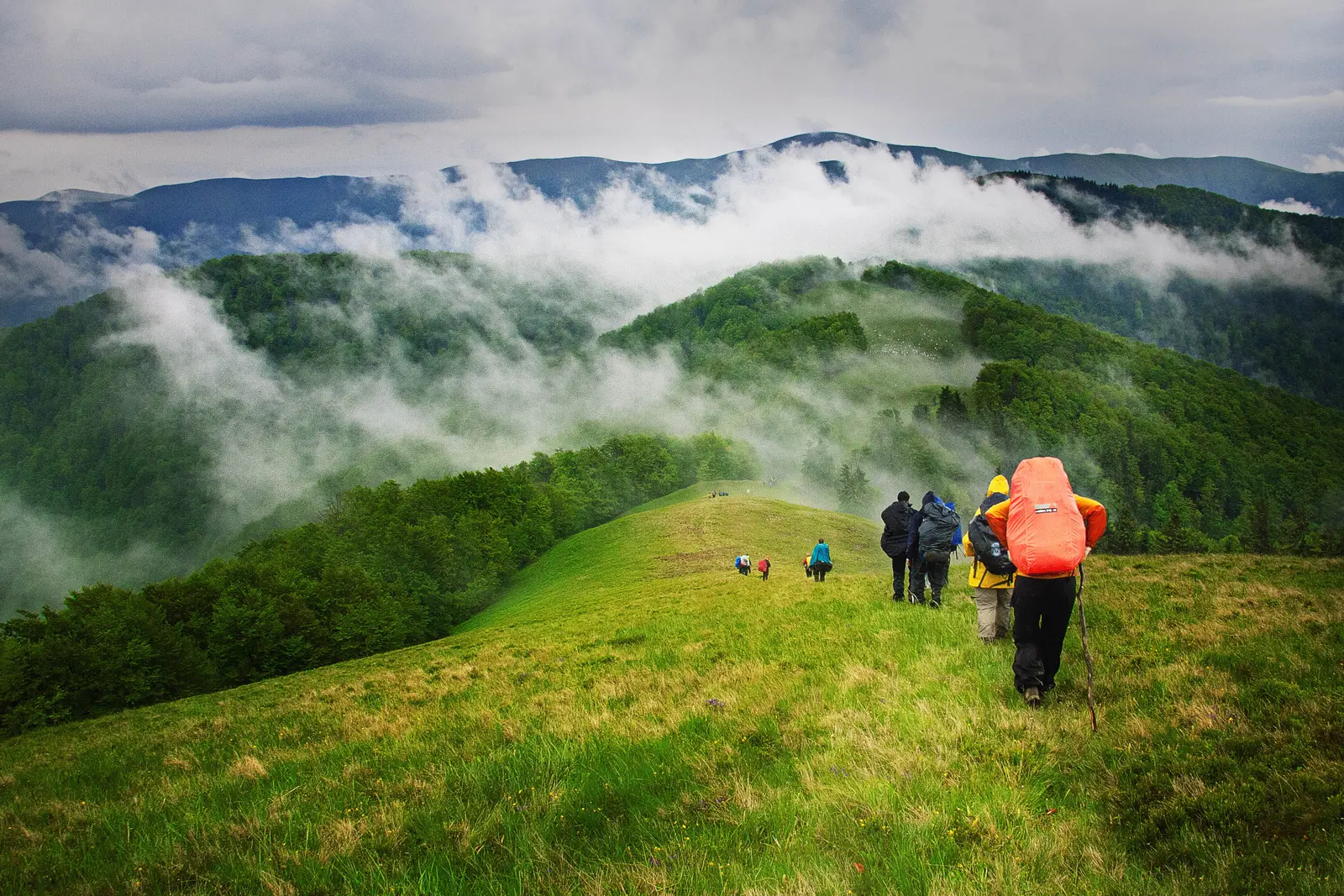 Exkursion Mehrere Menschen laufen mit Wandergepäck hintereinander auf einem Bergkamm.