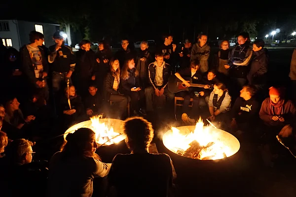 Menschen sitzen am Lagerfeuer, eine Person spielt Gitarre