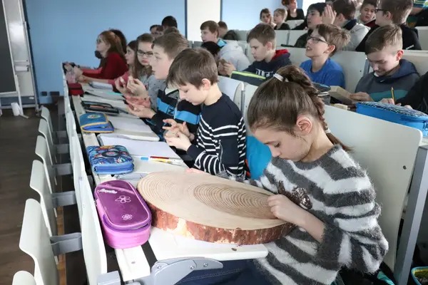 KinderUni Barnim Uckermark 2019 Schulkinder sitzen im Hörsaal und begutachten eine Holzscheibe. Ein Mädchen zählt die Jahrringe.