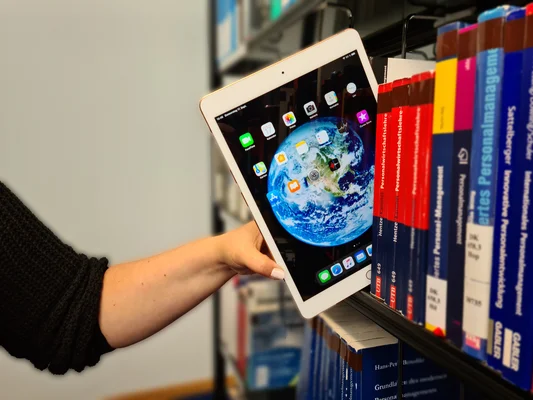 Bibliothek Ein Tablet wird ähnlich einem Buch in ein Bücherregal einer Fachbibliothek gestellt.