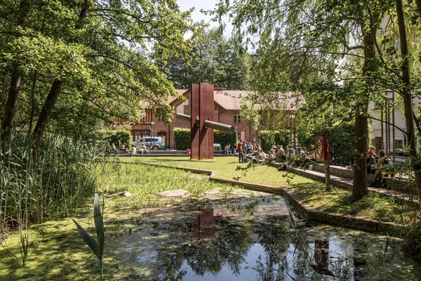 HNEE city campus with students and the sculpture ‘Die Durchdringung’ Auf dem Stadtcampus befindet sich ein Teichbiotop, moderne Kunst und Hochschulgebäude in diversen Baustilen.