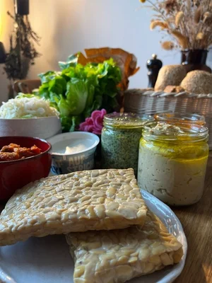 Zutaten für ein von Studierenden entwickeltes Tempeh-Brötchen Tisch mit der Sammlung an Zutaten für das Tempeh-Brötchen, das im Rahmen des Moduls „Studienpartner Ökobranche“ (2.FS) entwickelt wurde. Man sieht den Tempeh, Salat, verschiedene Aufstriche, Sauerkraut und die Brötchen.
