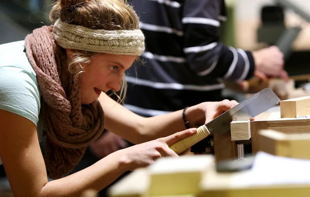 Eine Studentin fertigt ein Holzspielzeug an. Eine Studentin sägt mit der Japansäge ein Stück Holz ab.