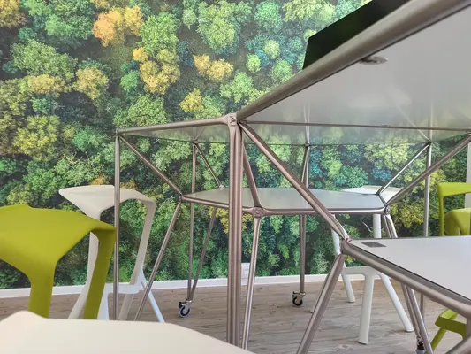 Futuristic tables and stools Futuristische Tische und Hocker sowie ein Waldmotiv aus der Vogelperspektive als Wanddekoration im Hintergrund.