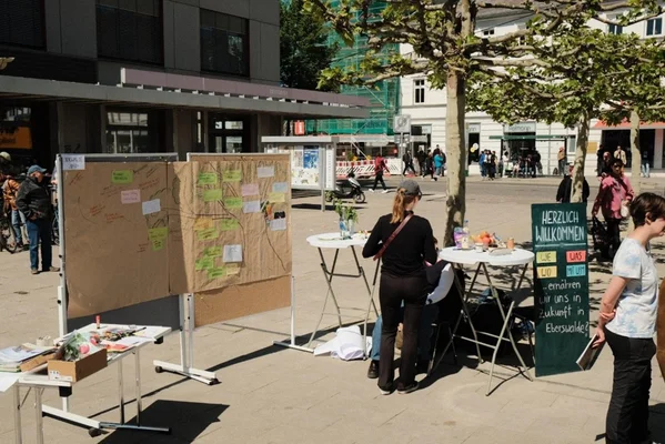 Intervention auf dem Marktplatz zur Identifikation von Visionselementen für eine zukünftige Ernährungskultur Set-Up einer Intervention auf dem Marktplatz im Rahmen des Moduls „Ernährungskulturen der Zukunft“ (4. FS). Man sieht das Begrüßungsschild, den Materialtisch und zentral den Traumbaum für die Visionselemente der BürgerInnen für die Ernährungskultur in Eberswalde 2040.