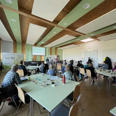 Planspiel Menschengruppen sitzen zusammen an Tischen und hören dem Redner zu