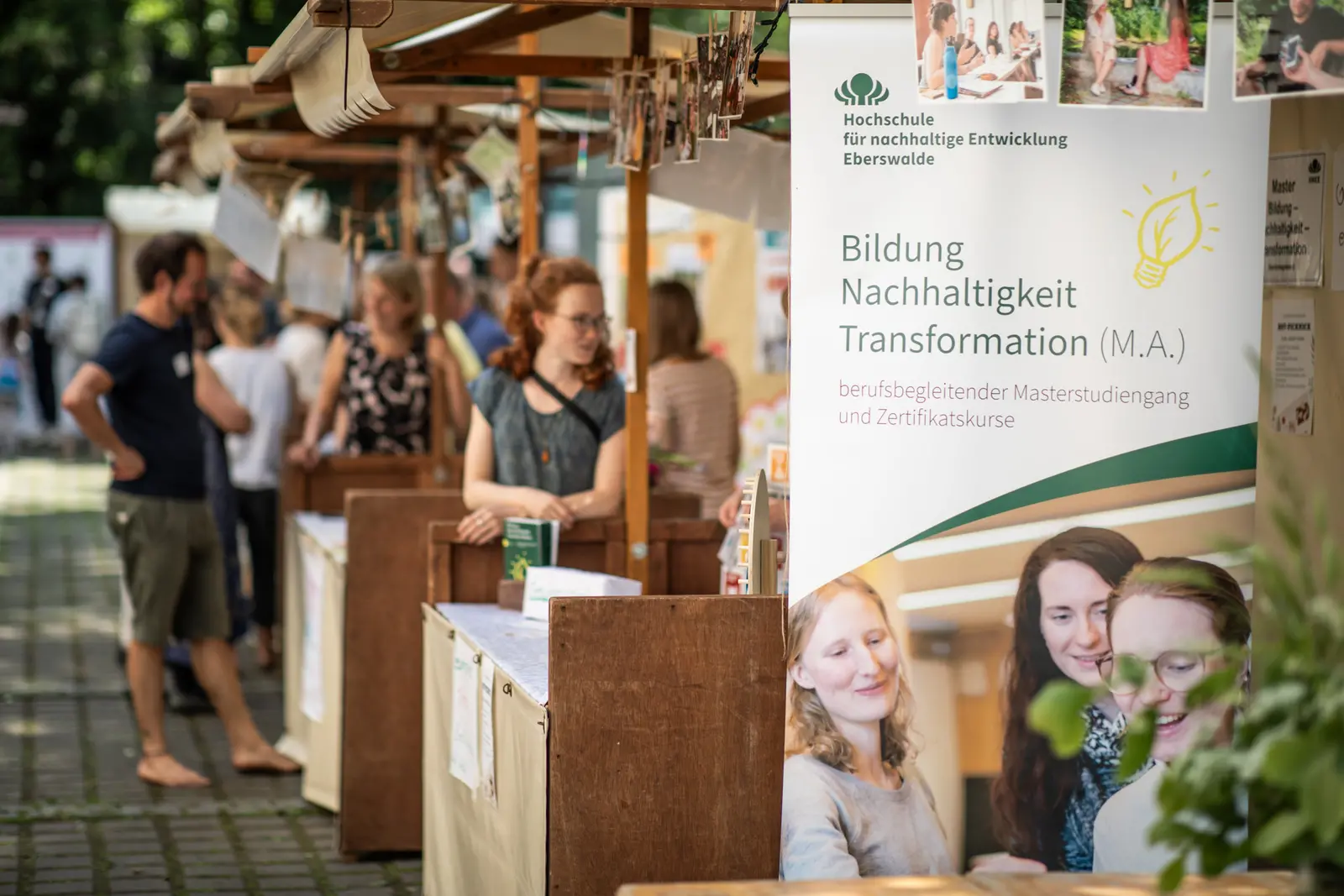 Bildung - Nachhaltigkeit - Transformation Im Vordergrund steht ein Roll-Up des Studiengangs Bildung - Nachhaltigkeit - Transformation , im Hintergrund sieht man Infostände und Personen.