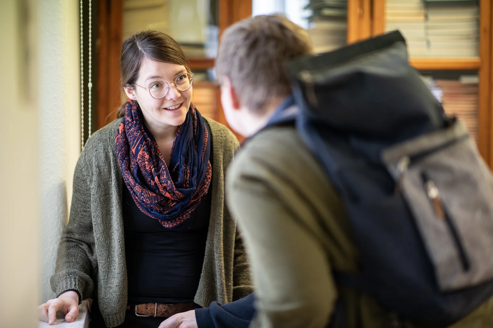 Studienorientierung der Präsenzstelle Das Bild zeigt zwei Personen in einem Gespräch während einer Veranstaltung zur Studienorientierung am Gymnasium. Eine Frau lächelt und trägt eine Brille, während sie mit einem Rucksack tragenden Jungen spricht.